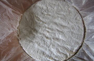 An unwrapped wheel of Brie de Meaux cheese on a wooden board