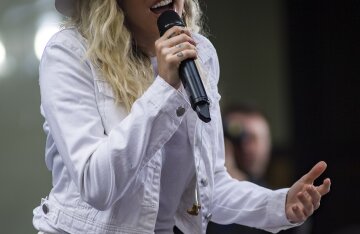 Miley Cyrus singing into a microphone outdoors on a talk show stage